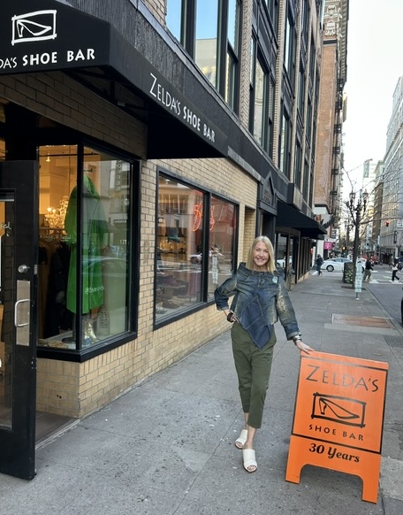 A smiling woman on the sidewalk beside the Zelda's Shoe Bar storefront and 30 Years sign in downtown Portland